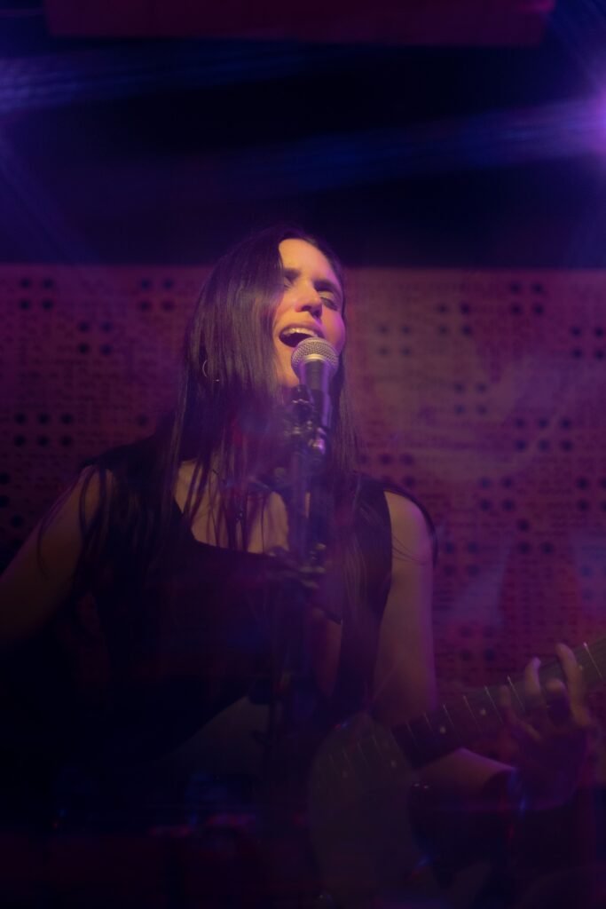 En la imagen podemos apreciar a la cantautora de PASKURANA cantando mientras toca la guitarra.