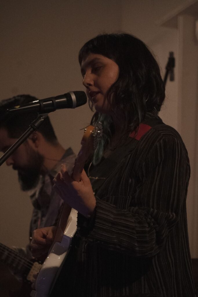 En la imagen se aprecia a la vocalista del grupo Alfilera cantando con una guitarra entre sus manos.